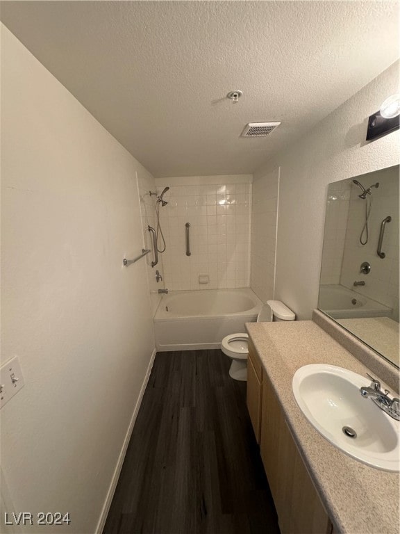 full bathroom with a textured ceiling, hardwood / wood-style floors, toilet, tiled shower / bath combo, and vanity