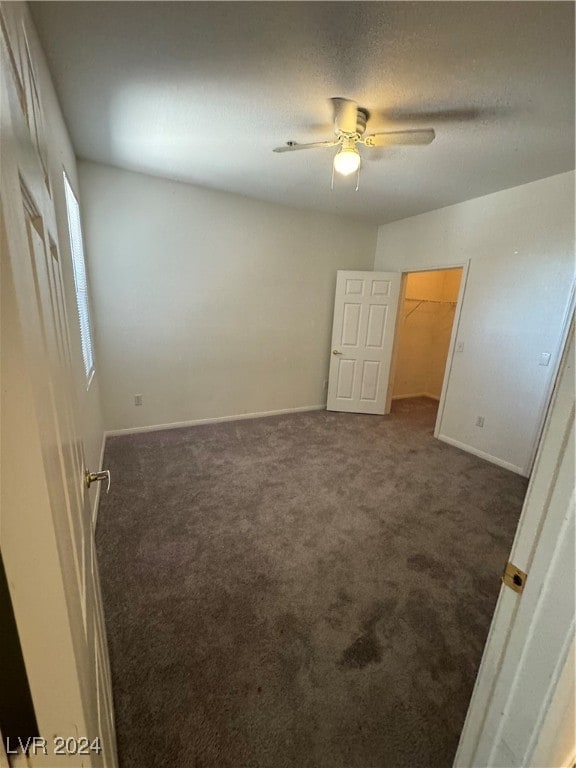 unfurnished bedroom featuring a walk in closet, ceiling fan, and carpet