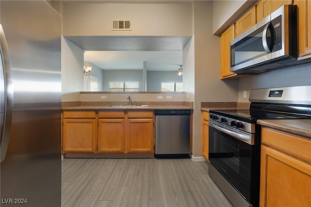 kitchen with light wood-type flooring, appliances with stainless steel finishes, sink, and ceiling fan