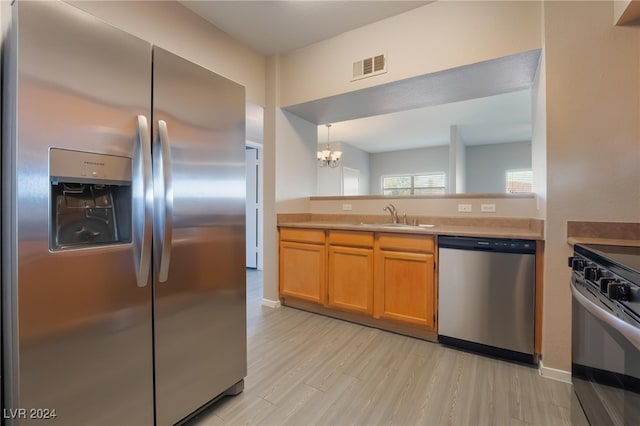 kitchen with stainless steel appliances, sink, an inviting chandelier, decorative light fixtures, and light hardwood / wood-style flooring