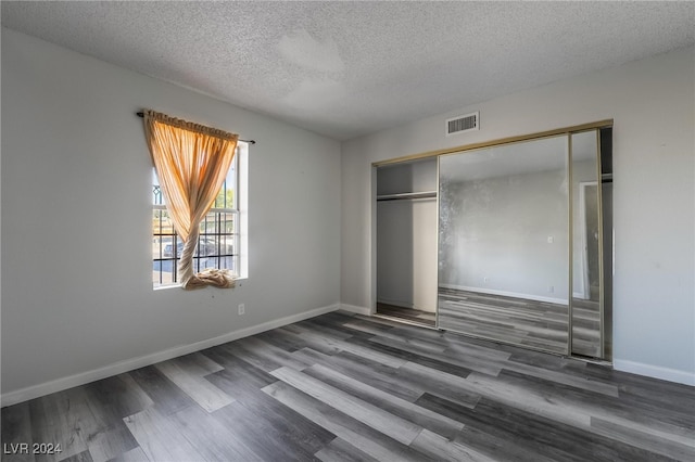 unfurnished bedroom featuring a textured ceiling, a closet, and dark wood-type flooring