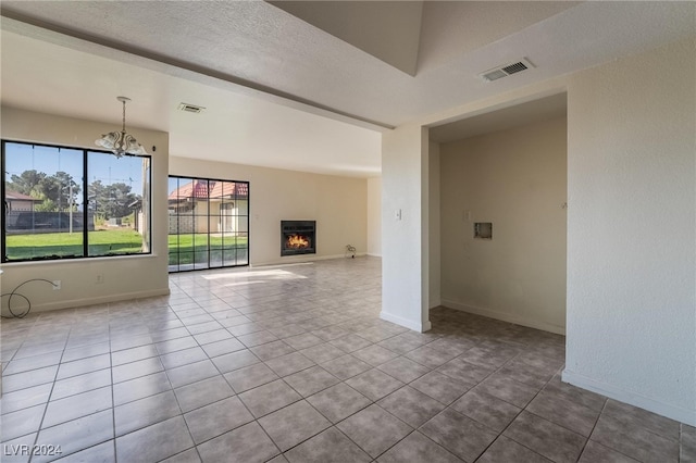 unfurnished living room featuring a textured ceiling, light tile patterned flooring, and a notable chandelier