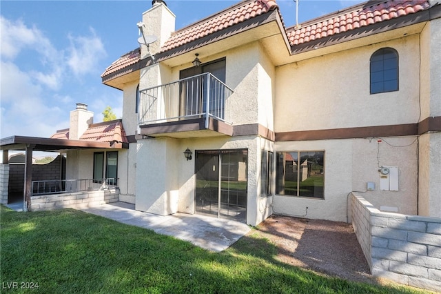 rear view of property with a balcony, a lawn, and a patio