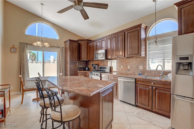 kitchen with sink, ceiling fan with notable chandelier, a kitchen island, appliances with stainless steel finishes, and a healthy amount of sunlight