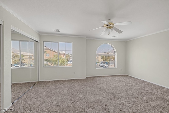 carpeted empty room featuring a wealth of natural light, crown molding, and ceiling fan