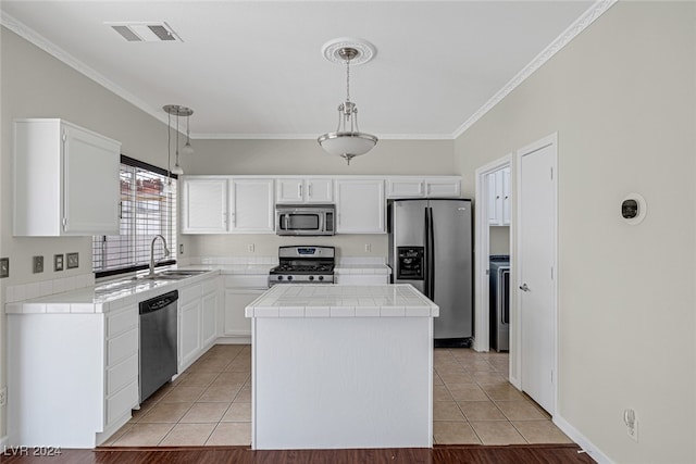 kitchen with appliances with stainless steel finishes, sink, white cabinetry, pendant lighting, and tile counters