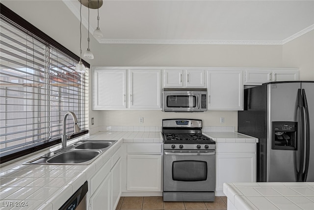 kitchen with appliances with stainless steel finishes, sink, decorative light fixtures, tile counters, and white cabinets