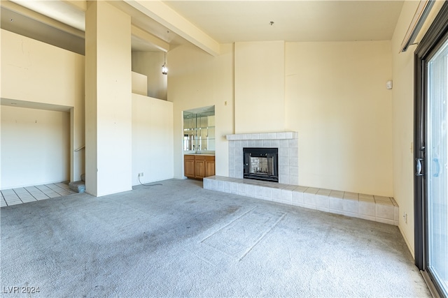 unfurnished living room with carpet, beam ceiling, and a tile fireplace