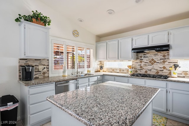 kitchen with a kitchen island, light stone countertops, appliances with stainless steel finishes, white cabinetry, and lofted ceiling