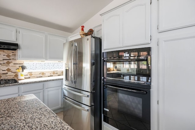 kitchen with backsplash, appliances with stainless steel finishes, light stone countertops, white cabinetry, and lofted ceiling