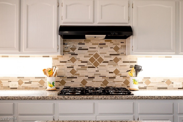 kitchen with black gas cooktop, decorative backsplash, light stone countertops, white cabinetry, and exhaust hood