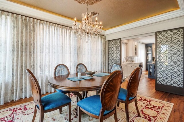 dining space featuring dark hardwood / wood-style floors, ornamental molding, a textured ceiling, a tray ceiling, and a chandelier