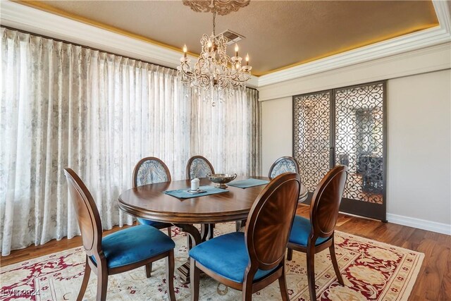 dining space with an inviting chandelier, crown molding, a textured ceiling, a tray ceiling, and wood-type flooring