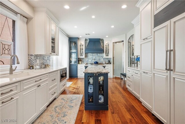 kitchen with premium range hood, white cabinets, sink, dark hardwood / wood-style floors, and a kitchen island