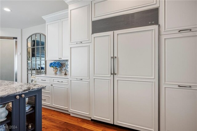 kitchen featuring hardwood / wood-style floors, white cabinets, paneled built in refrigerator, blue cabinetry, and light stone counters