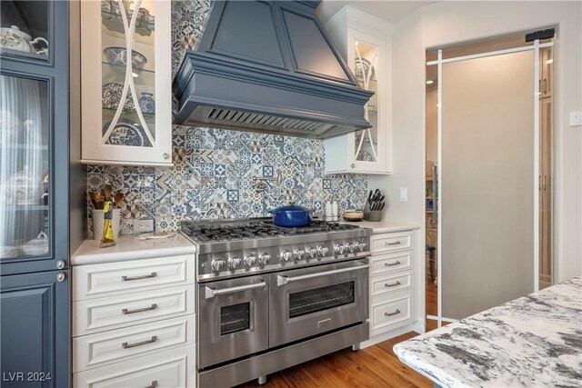 kitchen featuring custom exhaust hood, range with two ovens, white cabinetry, and tasteful backsplash