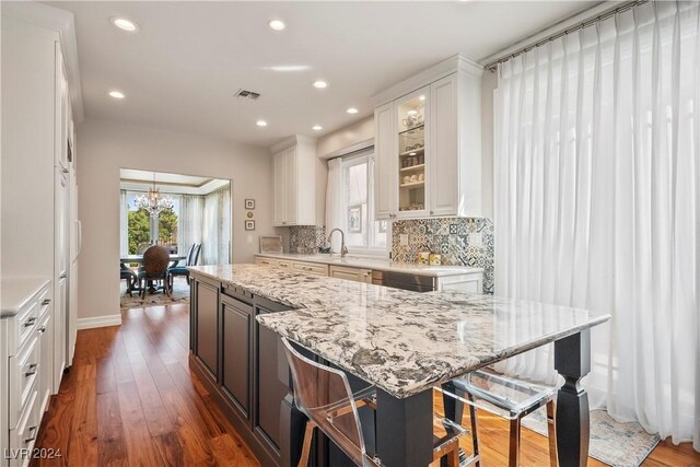 kitchen with decorative backsplash, light stone countertops, dark hardwood / wood-style flooring, a breakfast bar, and white cabinetry