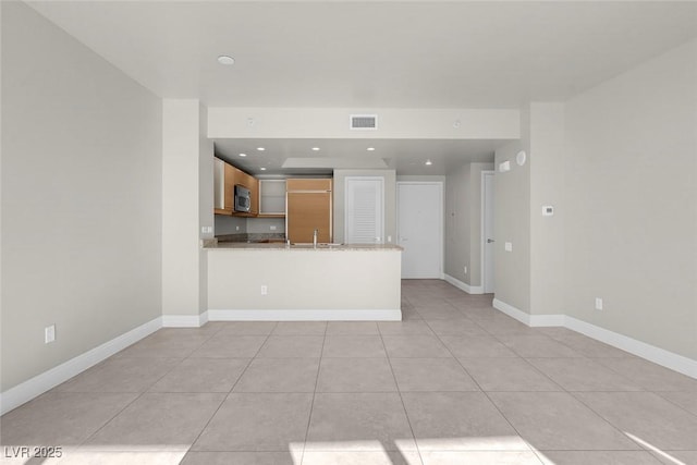 kitchen with light stone counters, kitchen peninsula, sink, and light tile patterned floors