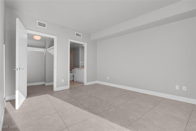 unfurnished bedroom with ensuite bathroom, light tile patterned floors, and a closet