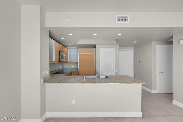 kitchen featuring sink, light stone counters, kitchen peninsula, black electric stovetop, and light tile patterned floors