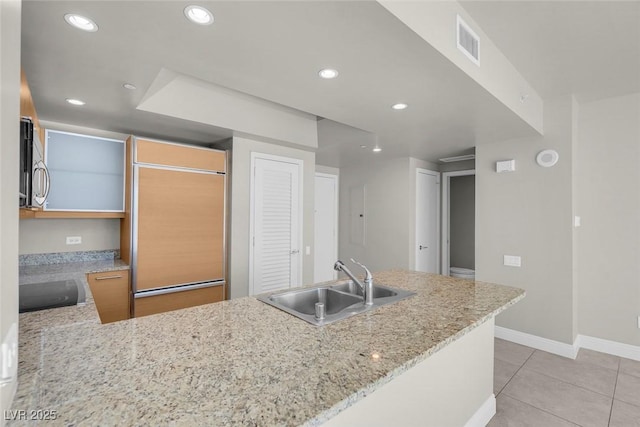 kitchen featuring paneled built in fridge, sink, light tile patterned floors, light stone counters, and kitchen peninsula