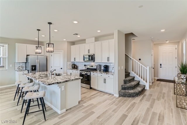 kitchen featuring light stone countertops, appliances with stainless steel finishes, an island with sink, light wood-type flooring, and white cabinets