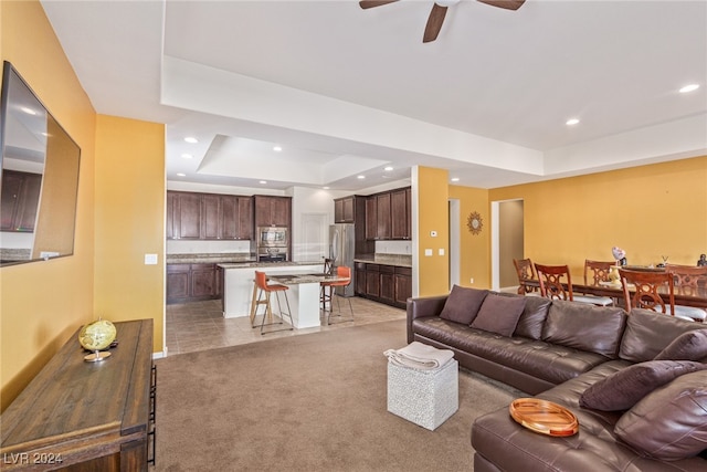 carpeted living room with ceiling fan and a raised ceiling