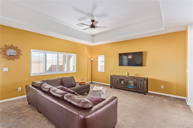 carpeted living room with a raised ceiling and ceiling fan