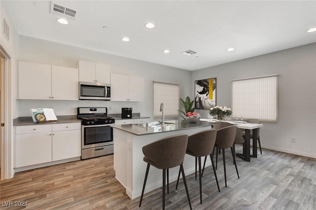 kitchen featuring sink, light hardwood / wood-style flooring, an island with sink, white cabinets, and appliances with stainless steel finishes