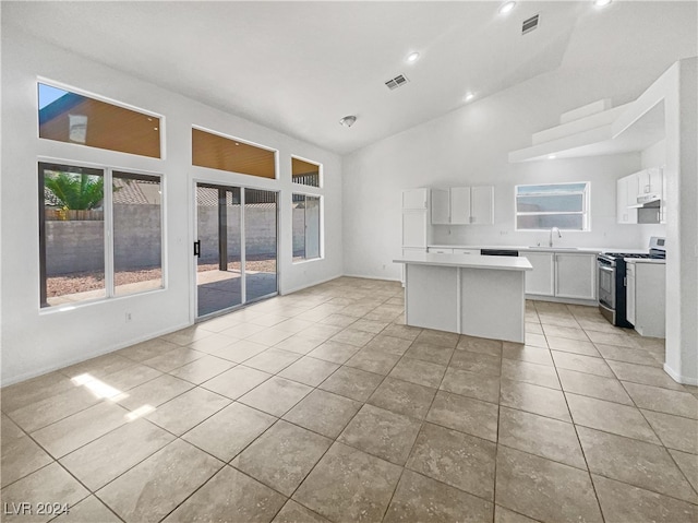 kitchen with lofted ceiling, a center island, stainless steel gas stove, and white cabinetry