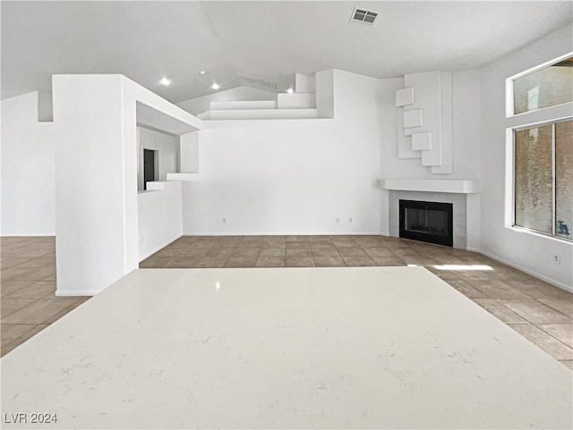 unfurnished living room featuring vaulted ceiling, a tiled fireplace, light tile patterned flooring, and a healthy amount of sunlight