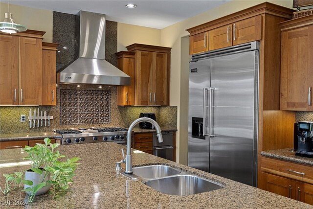 kitchen featuring appliances with stainless steel finishes, wall chimney exhaust hood, light stone counters, and backsplash