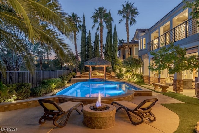 pool at dusk featuring an outdoor fire pit, a patio, and a gazebo