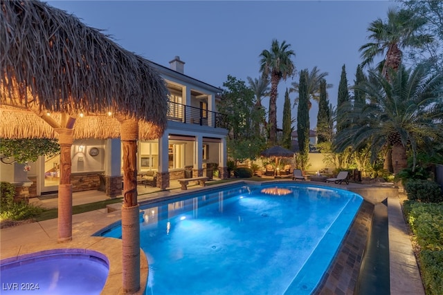 pool at dusk with a patio and a hot tub