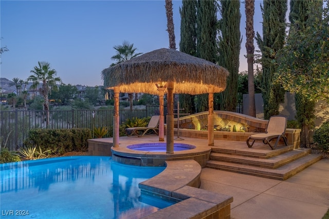 pool at dusk with an in ground hot tub and a gazebo