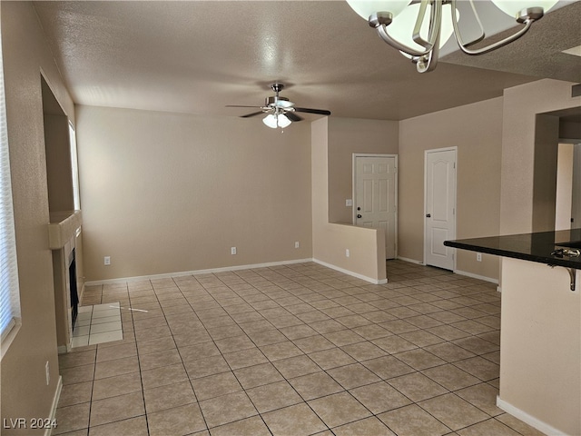 unfurnished living room with ceiling fan with notable chandelier, a textured ceiling, and light tile patterned flooring