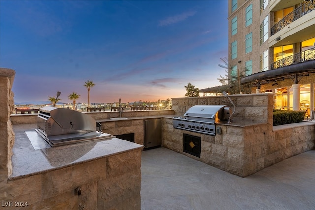 patio terrace at dusk with a balcony, exterior kitchen, grilling area, and sink