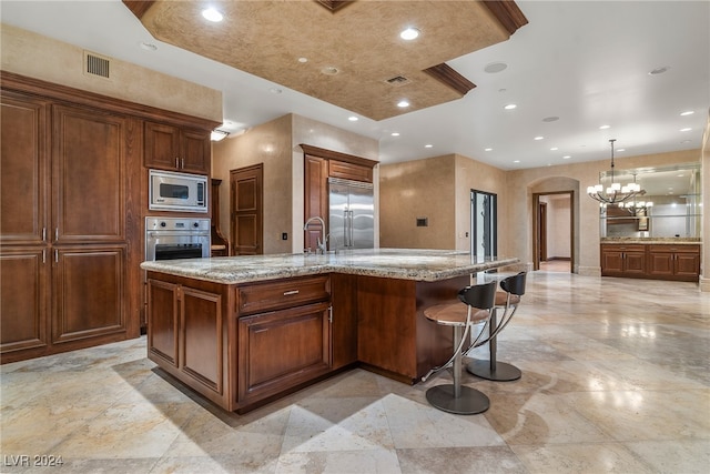 kitchen featuring pendant lighting, built in appliances, light stone counters, a breakfast bar area, and a large island