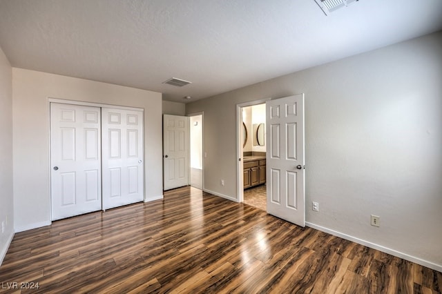 unfurnished bedroom featuring dark wood-type flooring, a textured ceiling, ensuite bathroom, and a closet