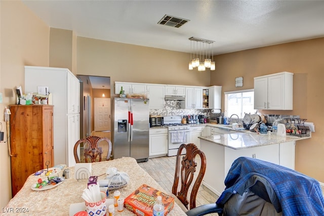 kitchen with hanging light fixtures, stainless steel fridge, kitchen peninsula, light wood-type flooring, and white gas range