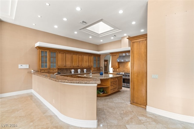 kitchen featuring stone countertops, kitchen peninsula, high end range, and extractor fan