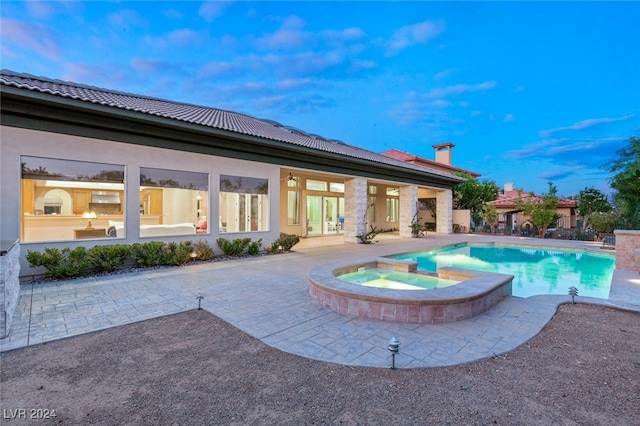 pool at dusk featuring an in ground hot tub and a patio