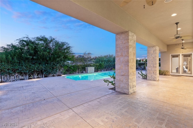 pool at dusk with ceiling fan and a patio