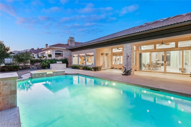 pool at dusk with ceiling fan and a patio area