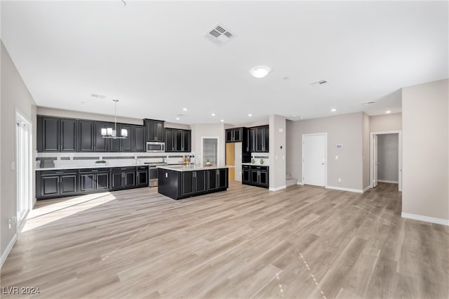 kitchen with pendant lighting, tasteful backsplash, light hardwood / wood-style flooring, a chandelier, and an island with sink