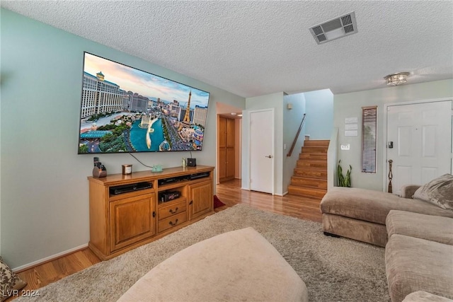 living room featuring baseboards, visible vents, stairs, light wood-style floors, and a textured ceiling