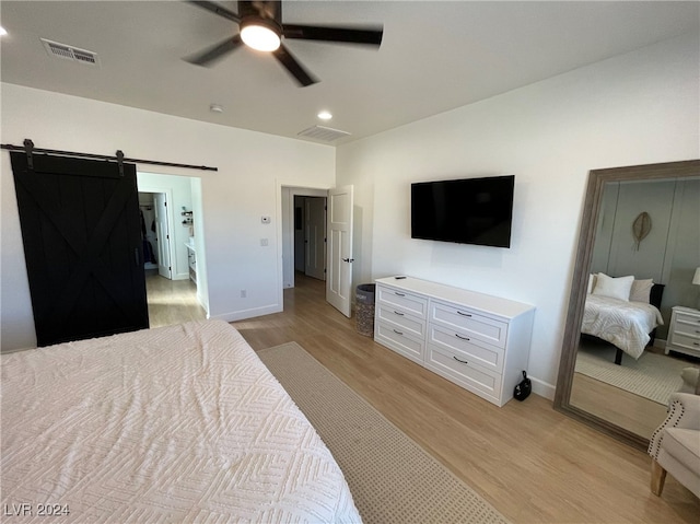 bedroom with a barn door, ceiling fan, and light hardwood / wood-style flooring