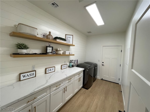 laundry area with washing machine and clothes dryer, light wood-type flooring, wood walls, and cabinets