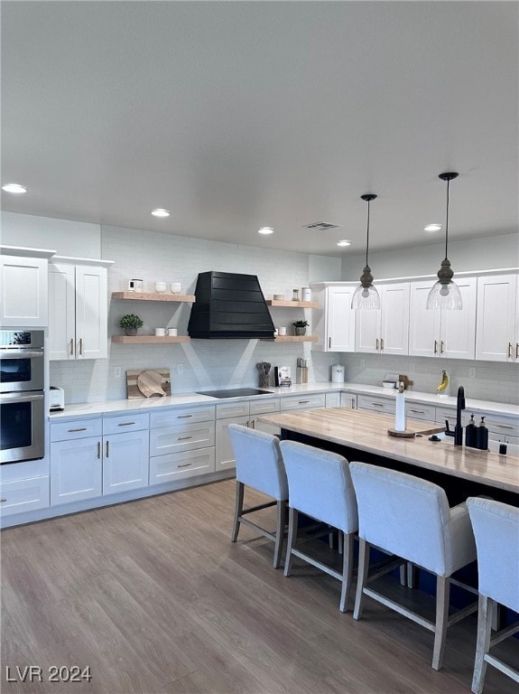 kitchen with white cabinetry, stainless steel double oven, exhaust hood, and hanging light fixtures