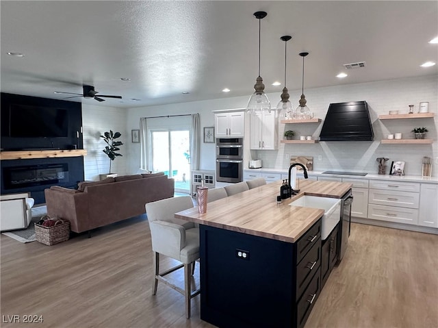 kitchen featuring white cabinets, ceiling fan, decorative light fixtures, a kitchen island with sink, and sink